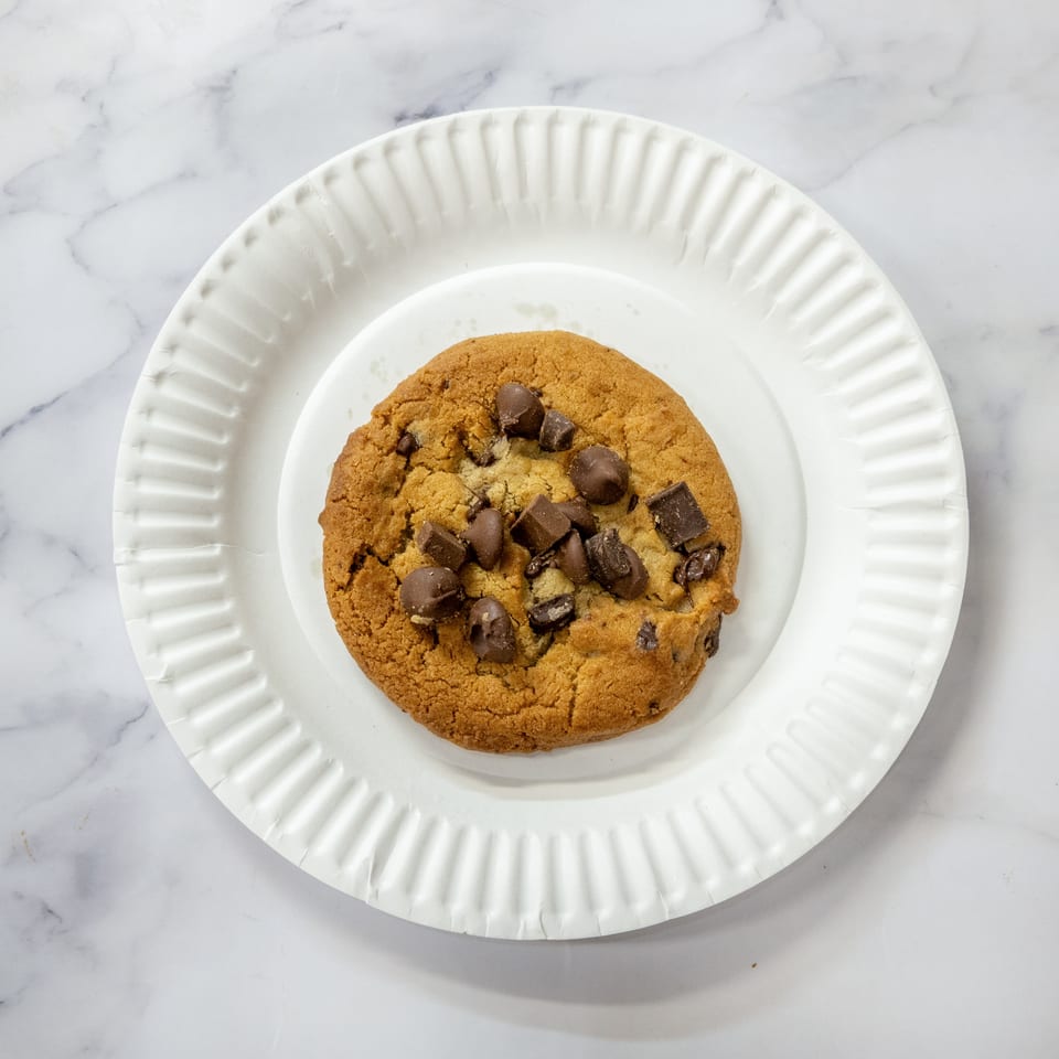 Chocolate chip cookie with large chocolate chunks on a white paper plate.