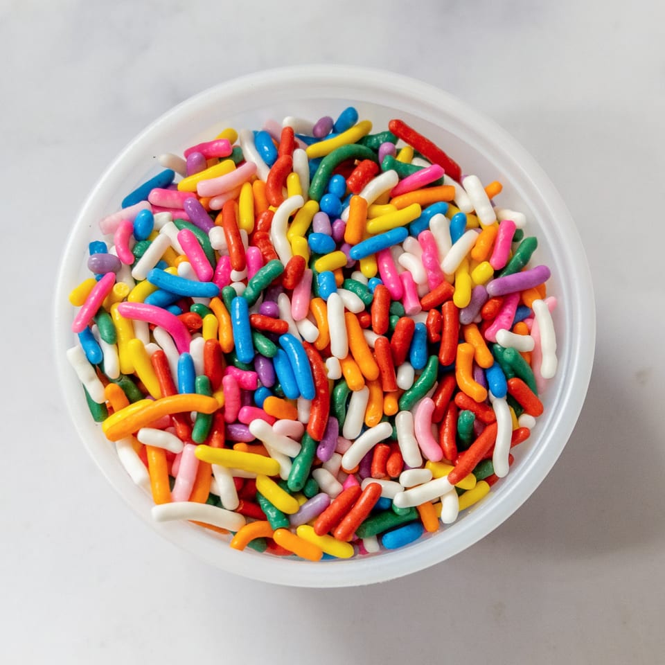 Overhead view of a white bowl overflowing with vibrant, multicolored sprinkles.