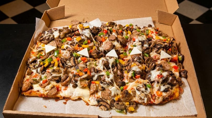 Rectangular pizza with sausage, mushrooms, and colorful bell peppers in a cardboard box.