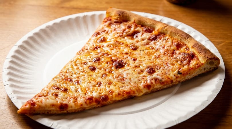 A single slice of cheese pizza with a golden crust on a white paper plate.
