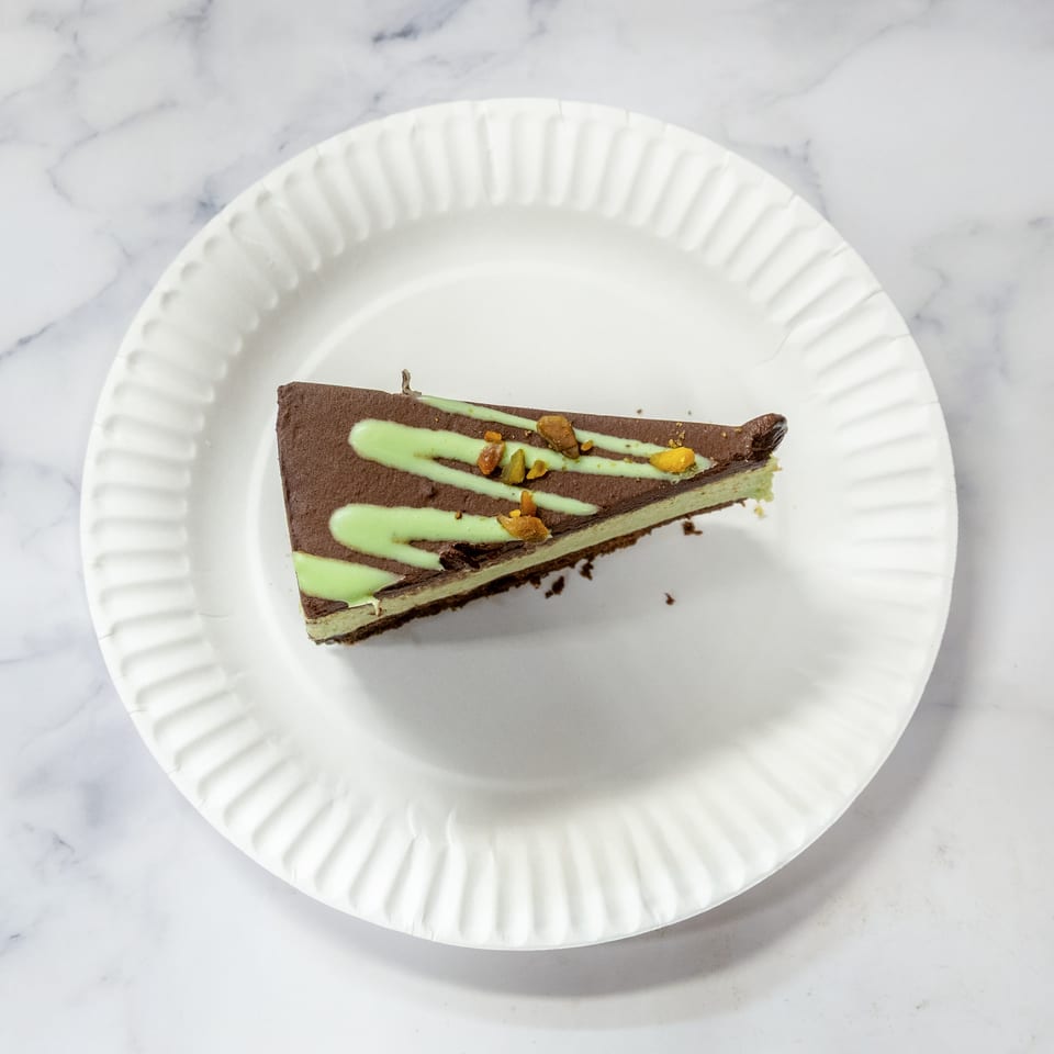 Slice of chocolate mint dessert with green icing swirls and chopped pistachios on a white paper plate.